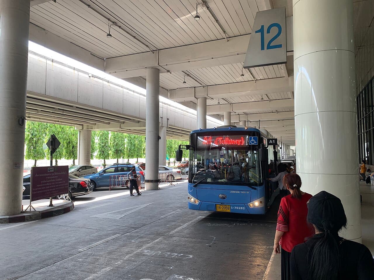 Bus station area at Don Mueang Airport with buses and passenger shelter.